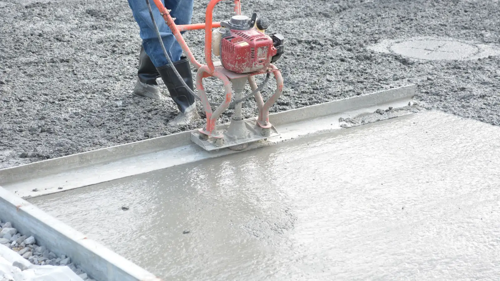 Pouring a concrete slab: a worker levels fresh concrete with a vibrating screed